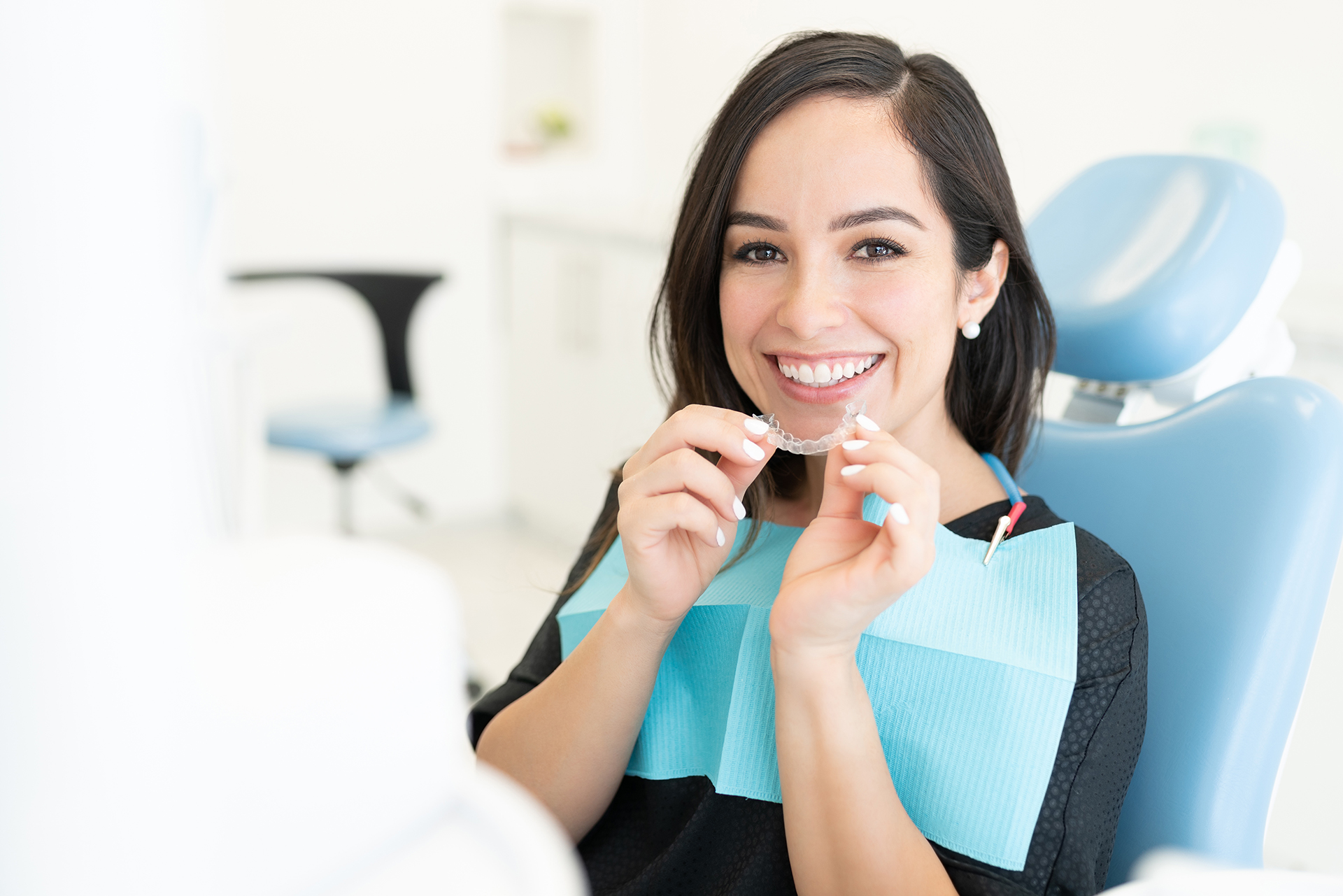 A woman sitting at a dental chair with a smile, holding a toothbrush in her hand.